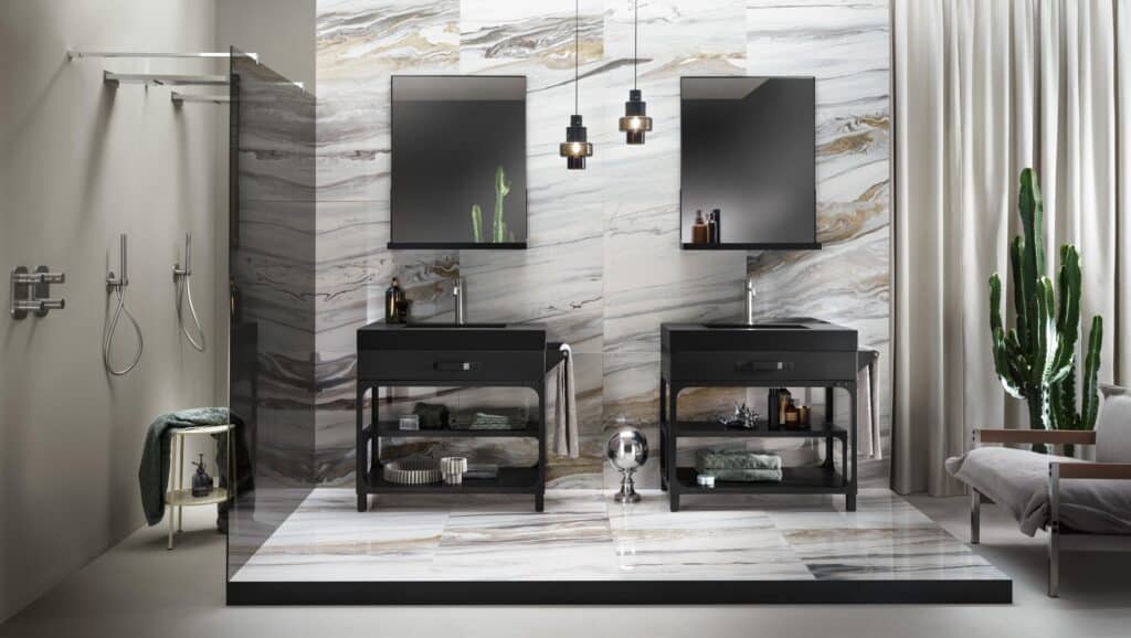 Modern bathroom with marble walls, dual sinks with black vanities, mirrors, pendant lights, a cactus plant, and a glass shower enclosure.