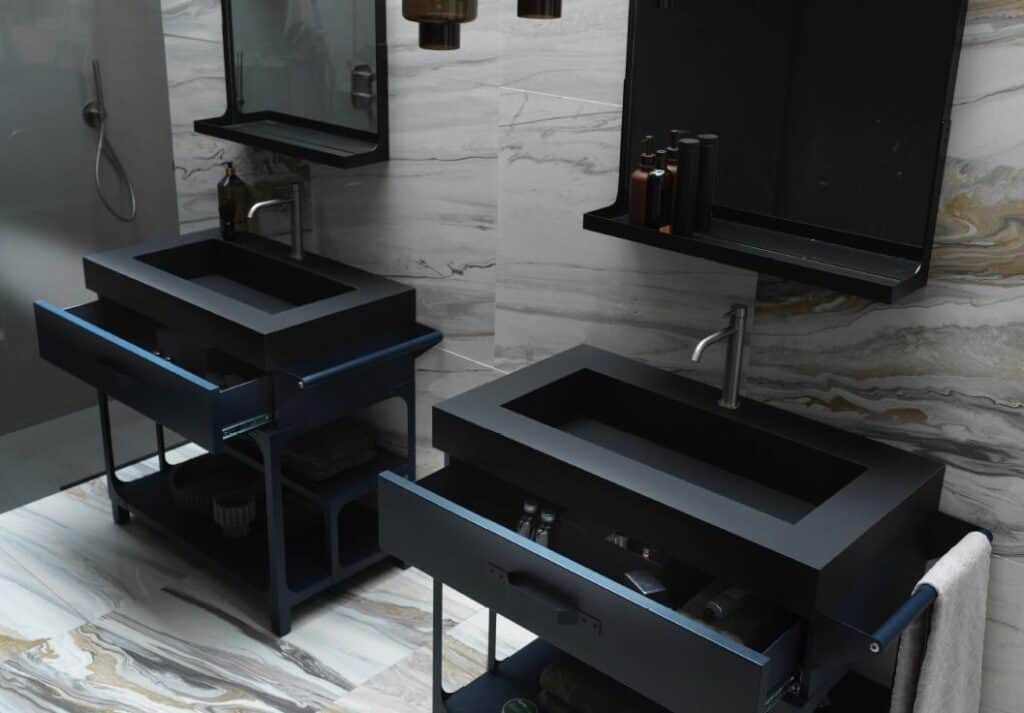 Modern bathroom with two black rectangular sinks, mounted on dark blue drawers, against marbled wall tiles.