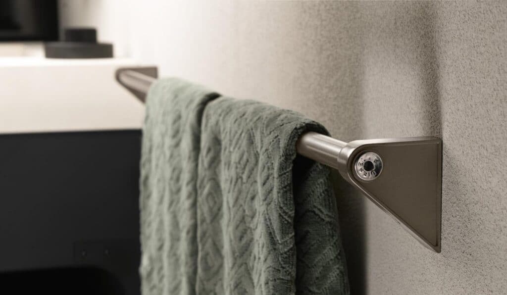 Silver towel rack with a textured green towel hanging on it, mounted on a light-colored wall.