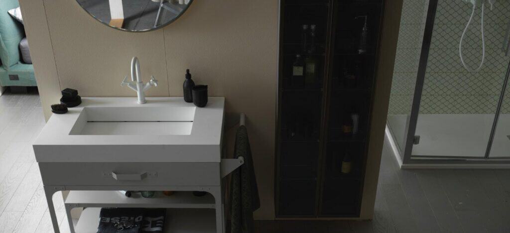 Modern bathroom with a white vanity sink, round mirror, shower, and a cabinet.