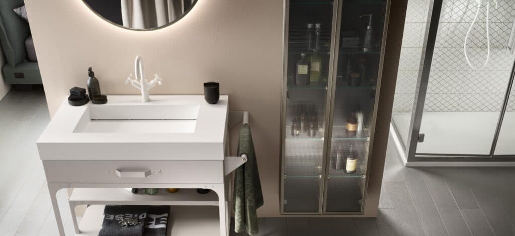 Modern bathroom with a white sink and countertop, round mirror, towel rack, storage shelf, and glass cabinet with toiletries.
