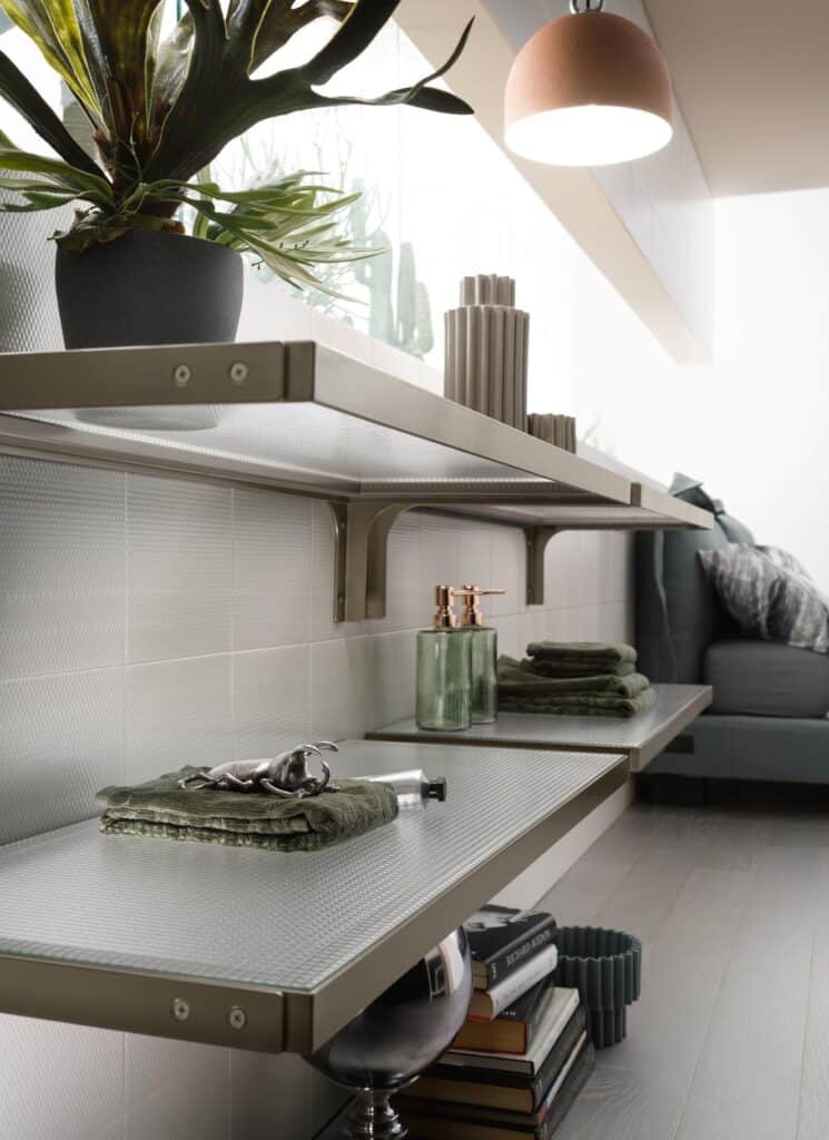 Modern interior with wall-mounted shelves, plants, folded towels, books, and decorative items, including a lamp and a glass container.