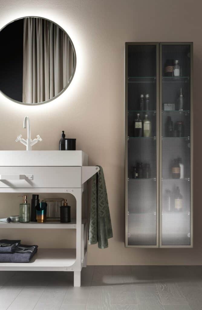 Modern bathroom with a round lighted mirror, white sink, and storage cabinet with frosted glass doors.