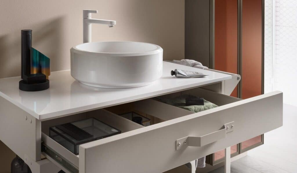 A modern bathroom vanity with a round white vessel sink, a minimalist faucet, and an open drawer revealing stored items.