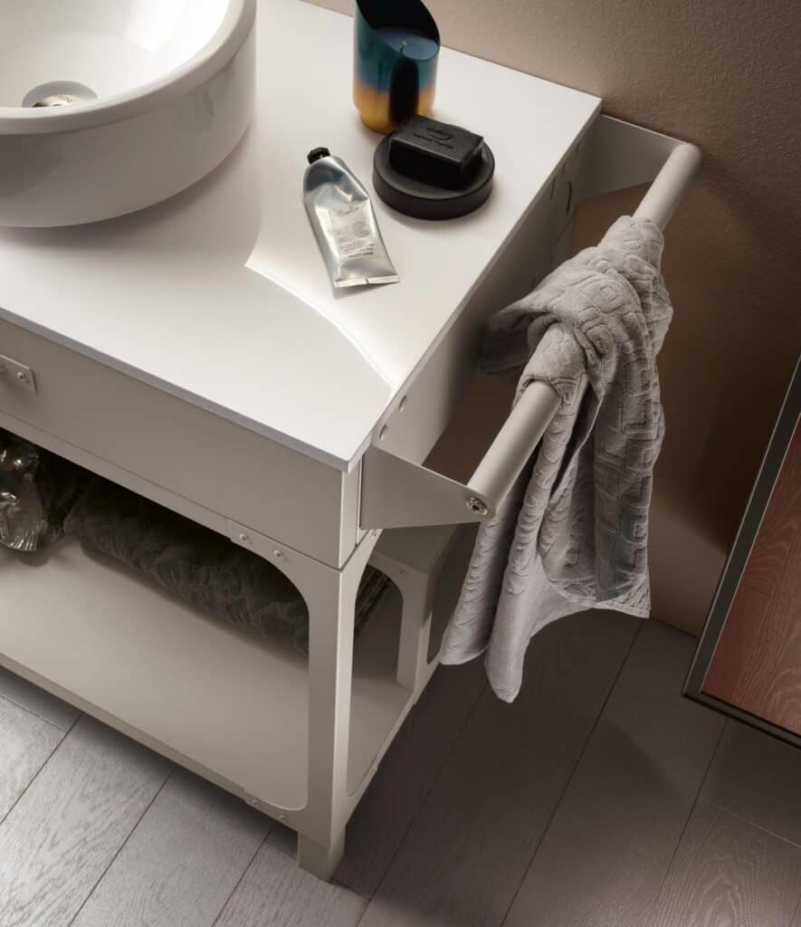 Modern bathroom vanity with a round sink, towel rack, candle, and toiletries on a white countertop.