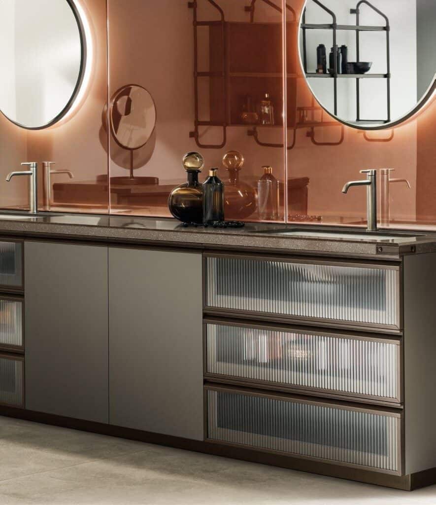 Modern bathroom vanity with a taupe-colored countertop, two round mirrors, sleek silver faucets, and decorative glass jars.