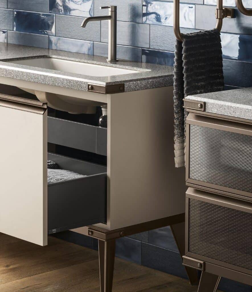 Modern bathroom vanity with metal legs, granite countertop, and a chrome faucet. The vanity has an open drawer and is set against a glossy blue tiled wall.
