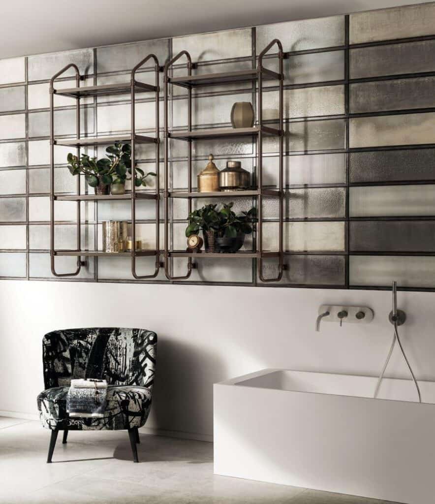 Modern bathroom interior with a black-patterned armchair, glass wall shelves holding plants and decor, and a white bathtub with wall-mounted fixtures.