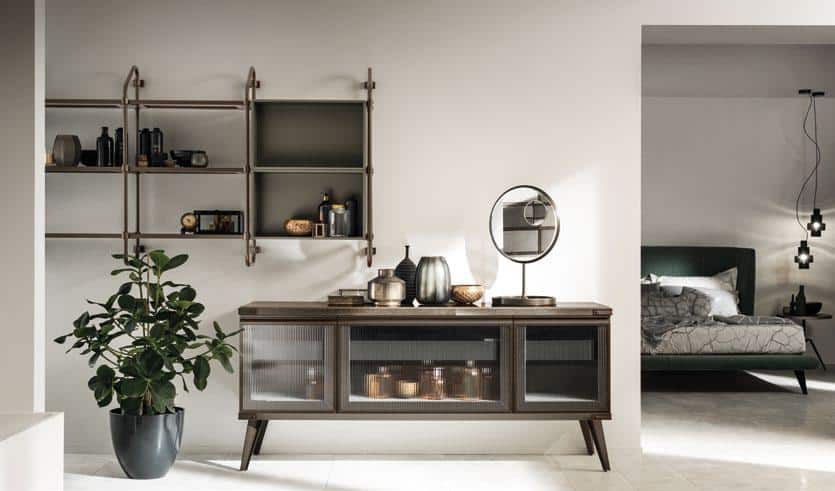 Modern dining area with a sleek sideboard, decorative items, a wall-mounted shelf, and a plant in the foreground. A bedroom is partially visible to the right.