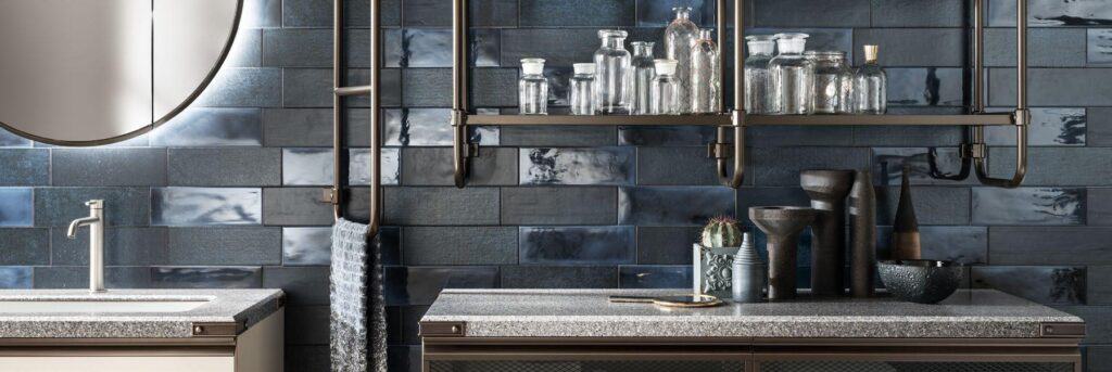 Modern kitchen with dark blue tile backsplash, glass jars on a metal shelf, a round mirror, and a textured countertop with a sink.