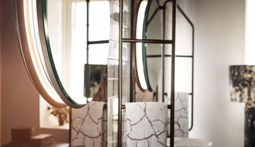 Modern bathroom with large illuminated round mirror, marbled wall panels, and windows in the background.
