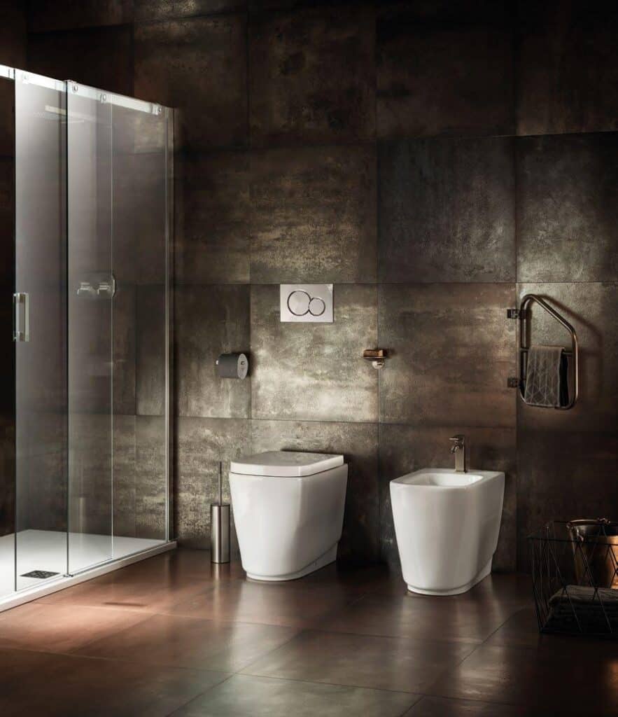 Modern bathroom with a glass shower, toilet, bidet, and metallic wall tiles.