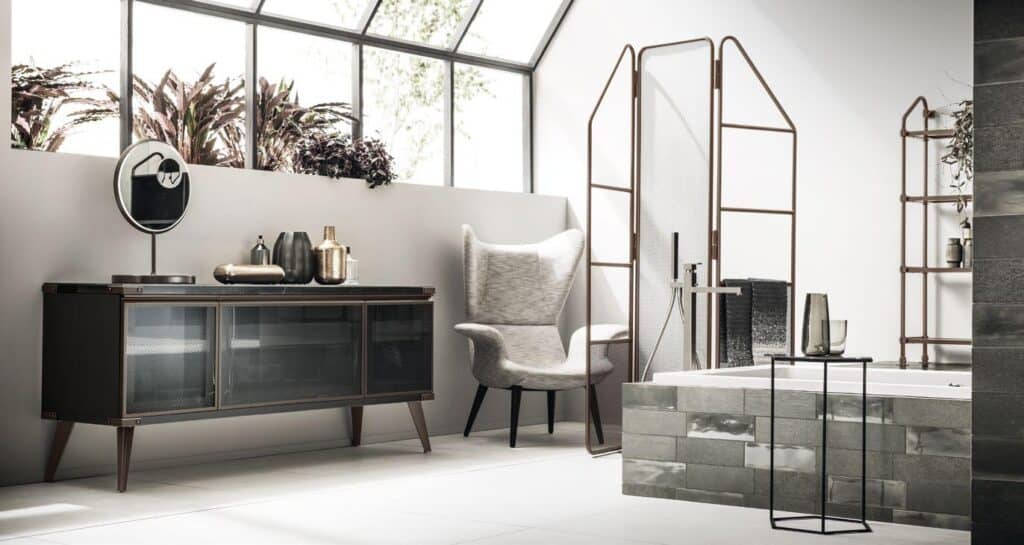 Modern bathroom with a large armchair, glass-front cabinet, decorative objects, and a bathtub with metal fixtures.