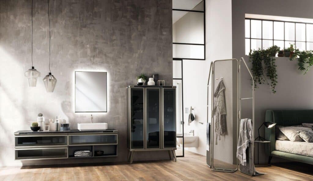 Modern bathroom interior with a gray textured wall, suspended vanity, mirror with backlighting, and two pendant lights. There&#039;s also a tall cabinet, indoor plants, and adjacent bedroom setup with a green bed and screen divider.