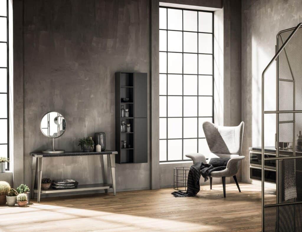 Modern industrial interior with large windows, a wingback chair, a console table with a mirror, and potted plants on a wooden floor.