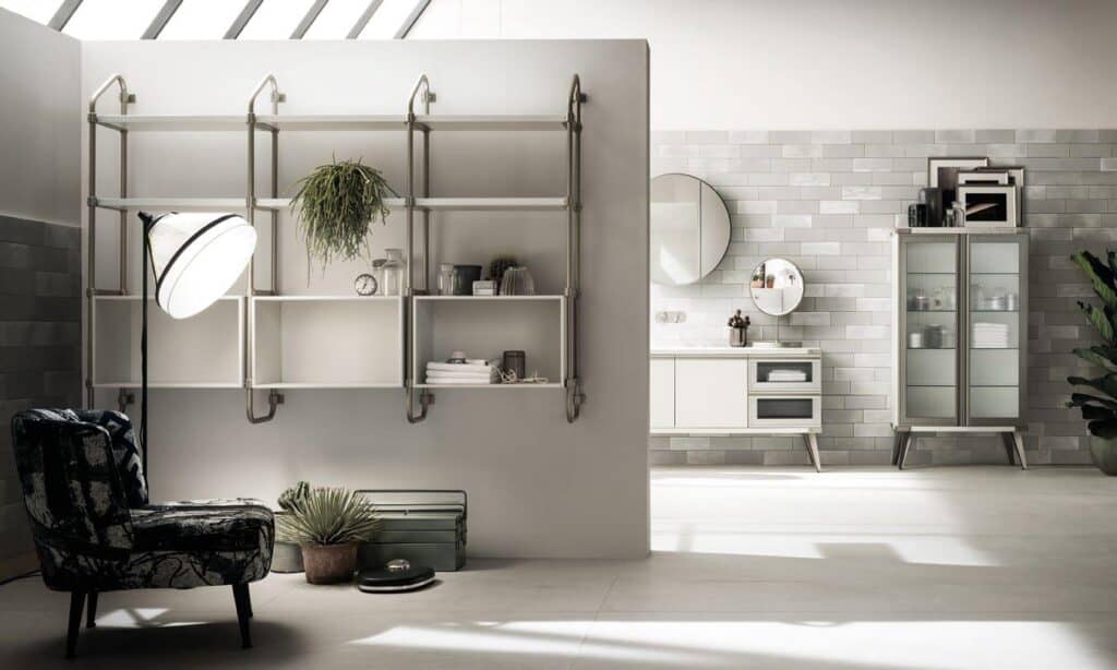 Modern interior with a chair, shelving, plants, and a lamp on the left; kitchen cabinets, mirrors, and a glass cabinet on the right, against a tiled wall.