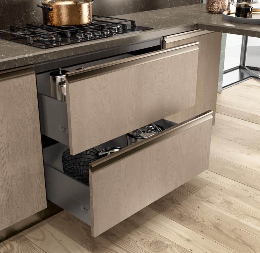 Modern kitchen with open wooden drawers under a countertop, containing kitchen utensils and pots.