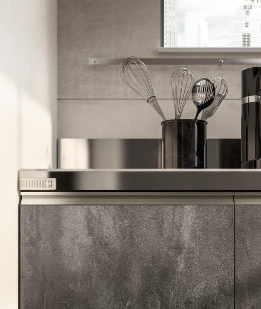 Modern kitchen with stainless steel countertop, textured gray cabinets, and a utensil holder containing whisks and a spoon.