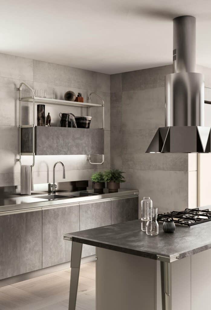 Modern kitchen with matte grey cabinetry, stainless steel fixtures, open shelves with decor items, a metallic range hood, and an island with a gas stove and glass bottles.