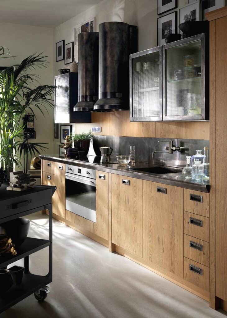 Modern kitchen with wooden cabinetry, stainless steel countertop, and two large rustic exhaust vents.