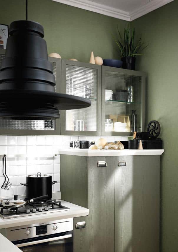 Modern kitchen with green walls, textured glass cabinets, a black hanging light, and stainless steel appliances.