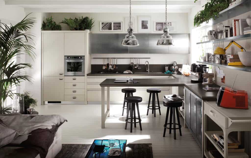 Modern kitchen with white cabinets, black countertops, and kitchen island with stools. Hanging metal lights, plants, and decor add a natural touch. Appliances and shelves with books and cookware enhance functionality.