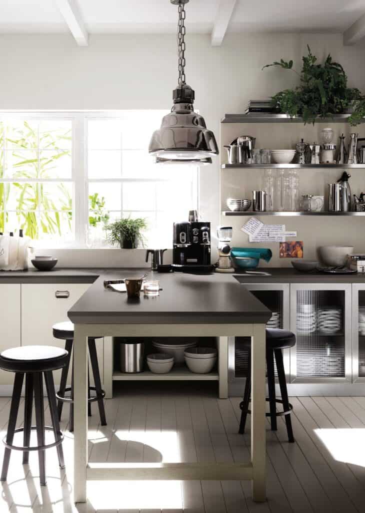 Modern kitchen with a central island, bar stools, hanging lamp, open shelves with utensils, a coffee machine, and plants by a window.