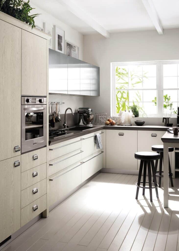 Modern kitchen with light wood cabinets, stainless steel appliances, a large window, and bar stools.