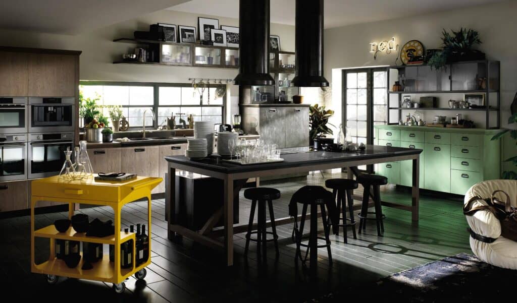Modern kitchen with a large island, yellow rolling cart, green cabinetry, and industrial-style decor.