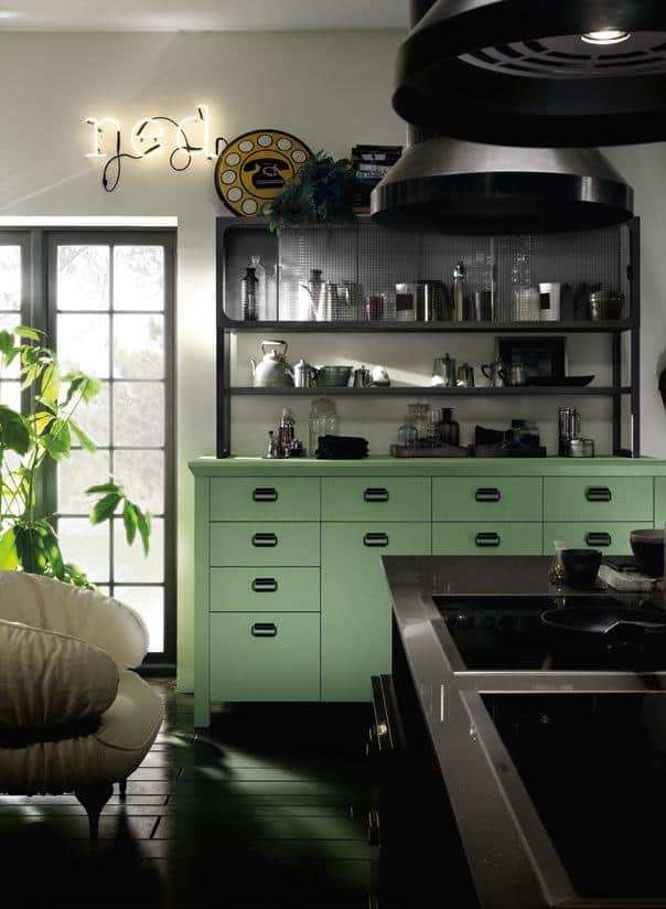 A stylish kitchen with a mint green cabinet and black countertops. Industrial shelves hold kitchenware, and a neon sign with &quot;hey&quot; hangs on the wall. A large plant is near the window, and overhead lights hang from the ceiling.