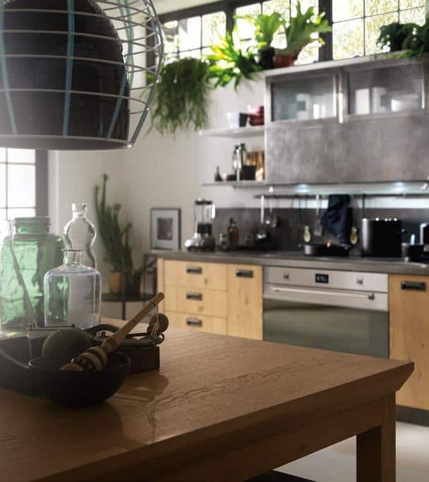Modern kitchen with wooden cabinets, green plants on shelves, a wooden table with kitchenware, and a metallic range hood.