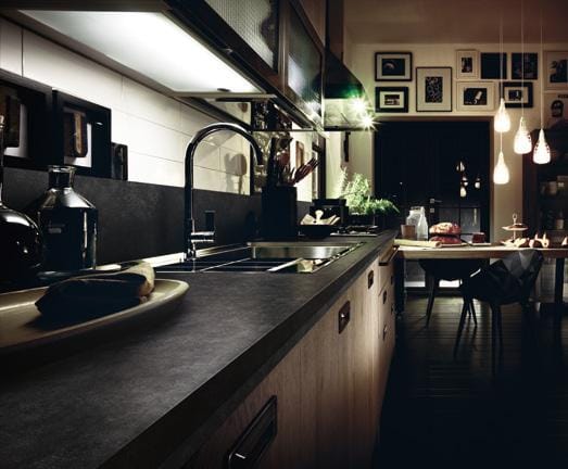 Modern kitchen interior with dark countertops, sleek cabinetry, a sink with a tall faucet, hanging pendant lights, and a dining area in the background.