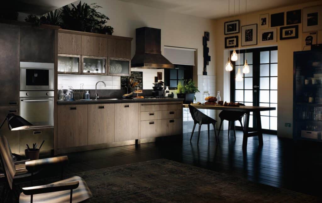 Stylish modern kitchen with wooden cabinets, a black countertop, and a dining table set with chairs. Hanging lights illuminate the table, and there are plants and decorative items throughout.
