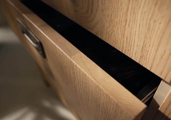 A close-up of a slightly open wooden drawer with a metal handle.