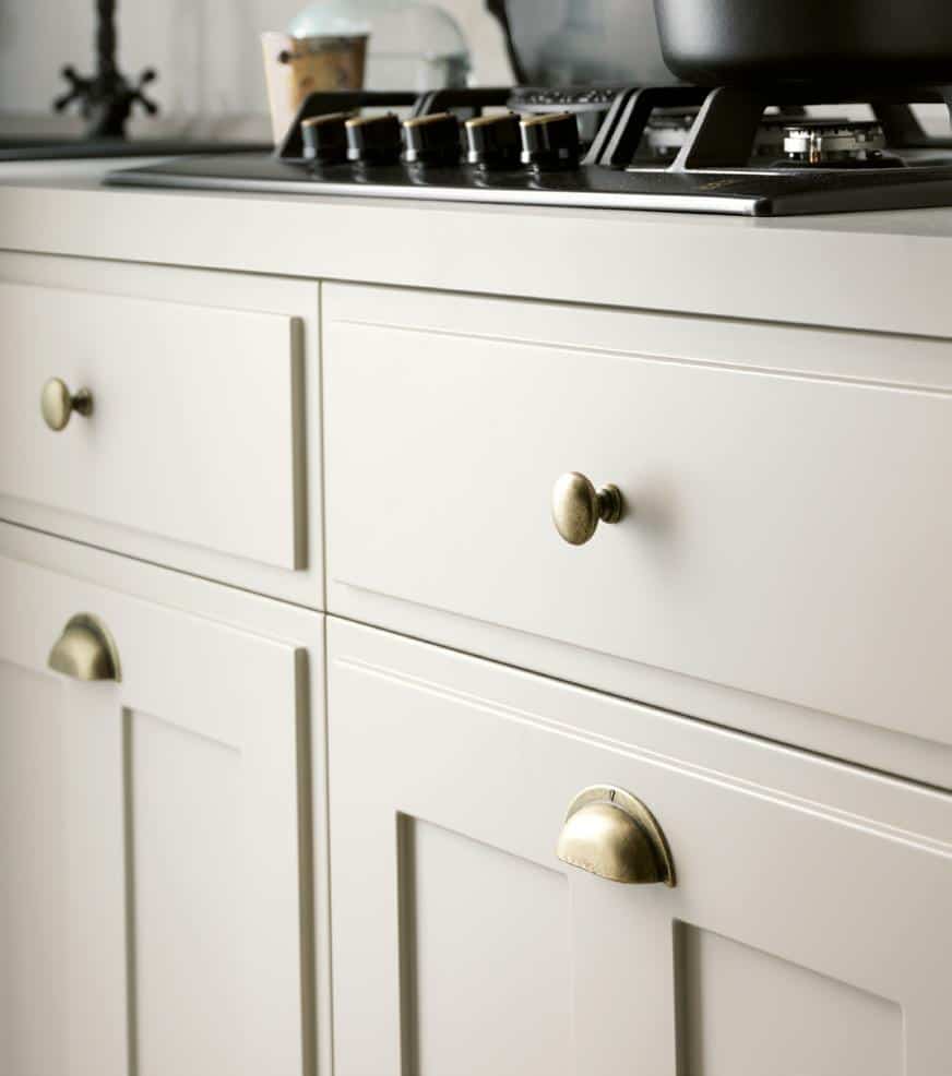 Close-up of a stove and white kitchen cabinets with brass handles.