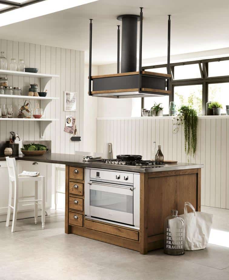 Modern kitchen with a central island featuring a built-in oven and stove, wooden cabinetry, minimalist shelves with jars, and a sleek ceiling-mounted vent hood, all set against light wooden paneling.