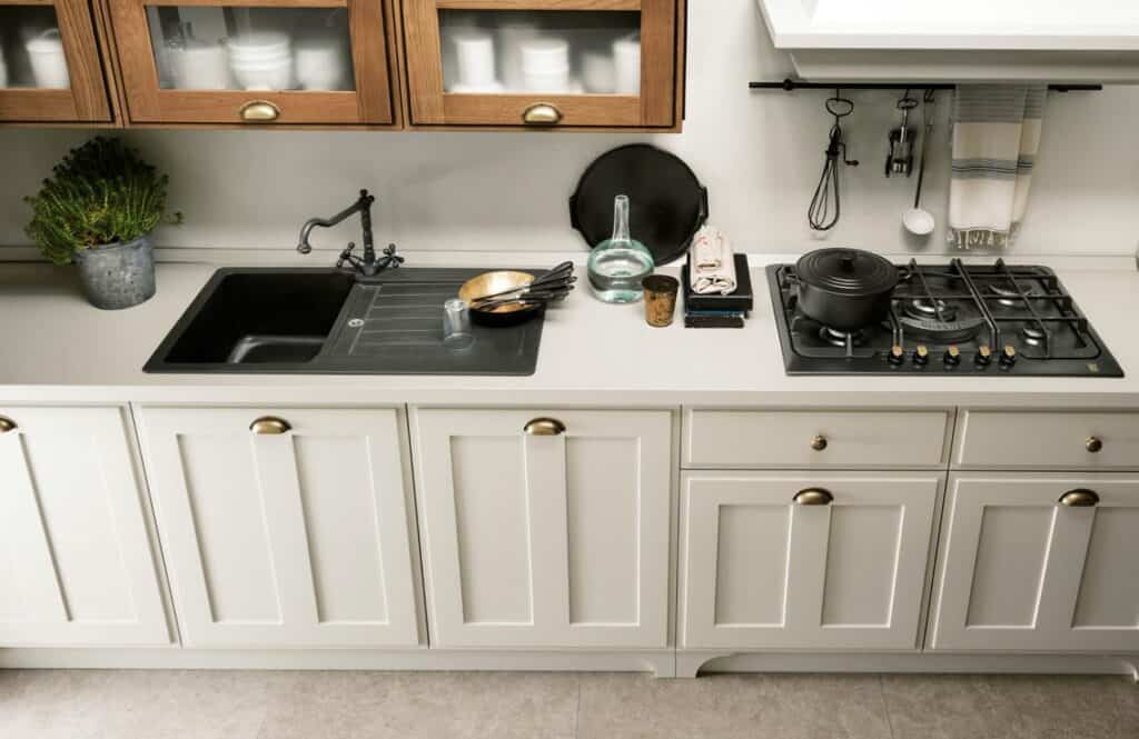 Kitchen countertop with a sink, glassware, cookware, potted plant, and a gas stove with a pot.