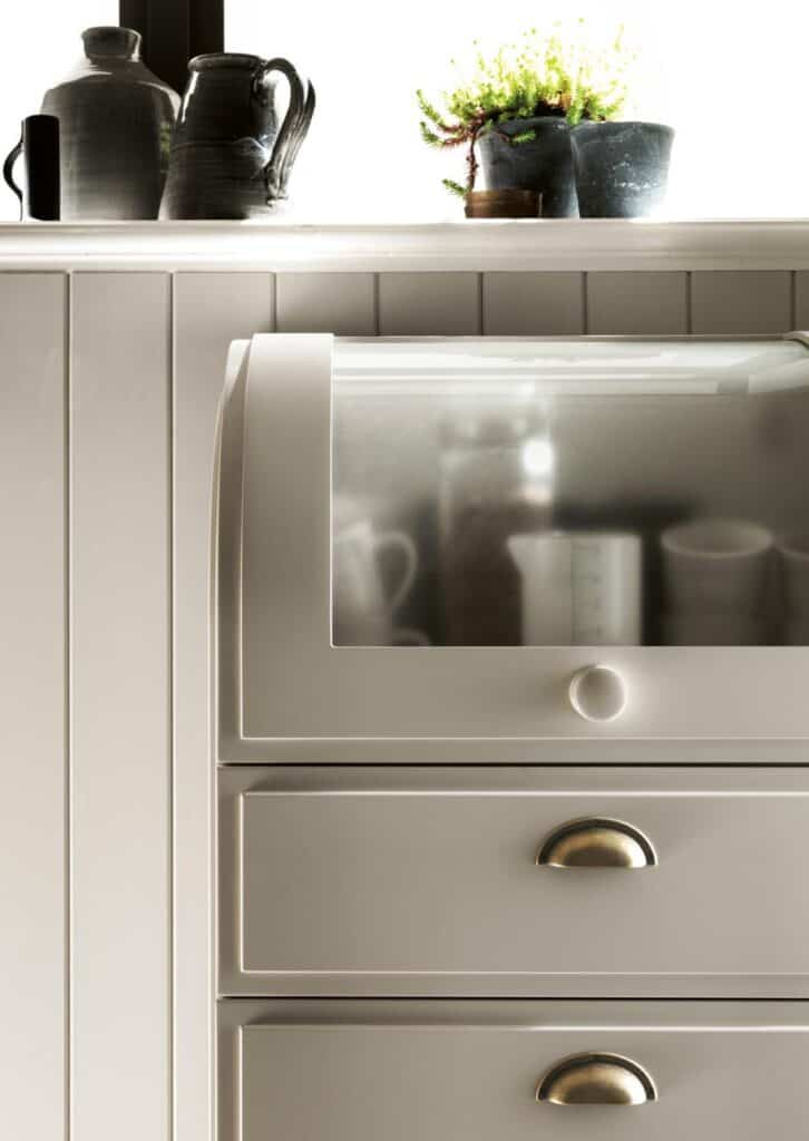 Kitchen cabinet with metallic handles, a frosted glass door, and ceramic jugs and potted plants on top.
