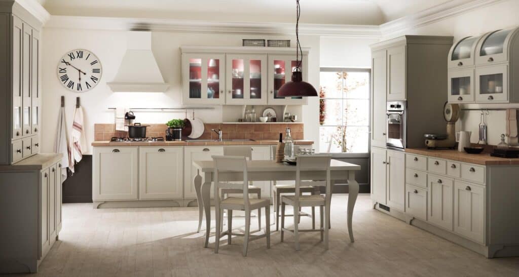 Spacious modern kitchen with white cabinets, a central dining table, a wall clock, and a large window allowing natural light.