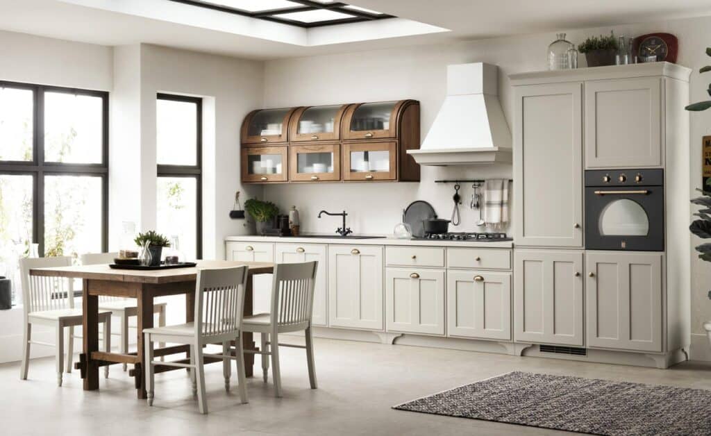 Modern kitchen with white cabinetry, wooden dining table, white chairs, and large windows.