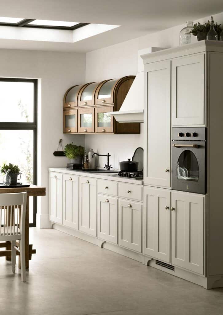 Modern kitchen with white cabinets, a built-in oven, and wooden upper cupboards under a skylight.