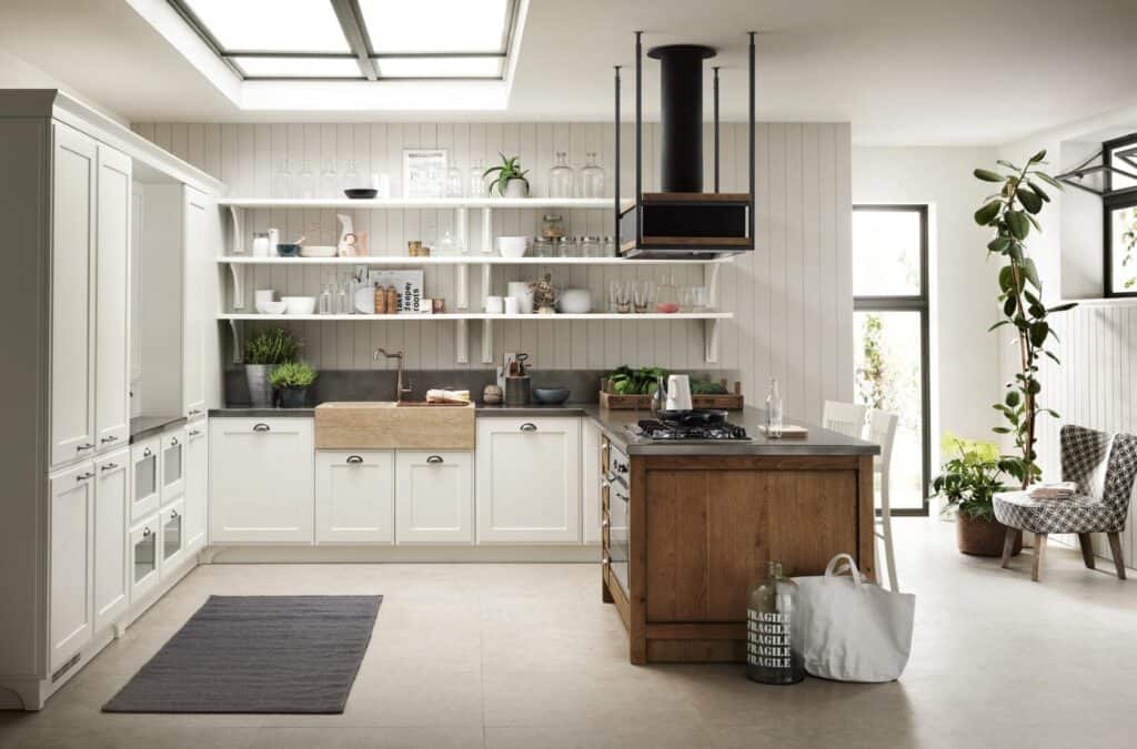Modern kitchen with light cabinetry, a large farmhouse sink, open shelves with decor, a wooden island with a stove, a skylight, and plants.