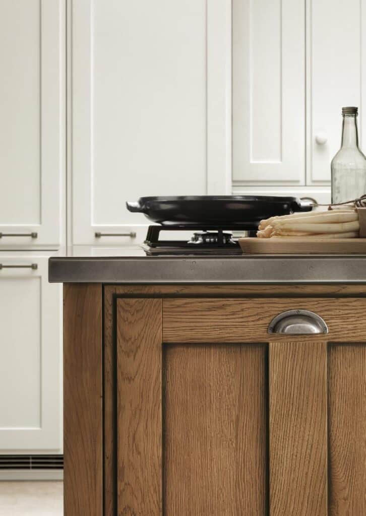 Kitchen counter with wooden cabinets, a black pan on a burner, and a bundle of asparagus next to a glass bottle.