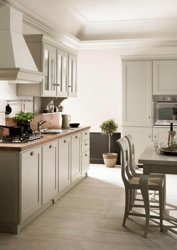 Modern kitchen with beige cabinetry, a central island with chairs, stainless steel appliances, potted plant, and wooden countertop.