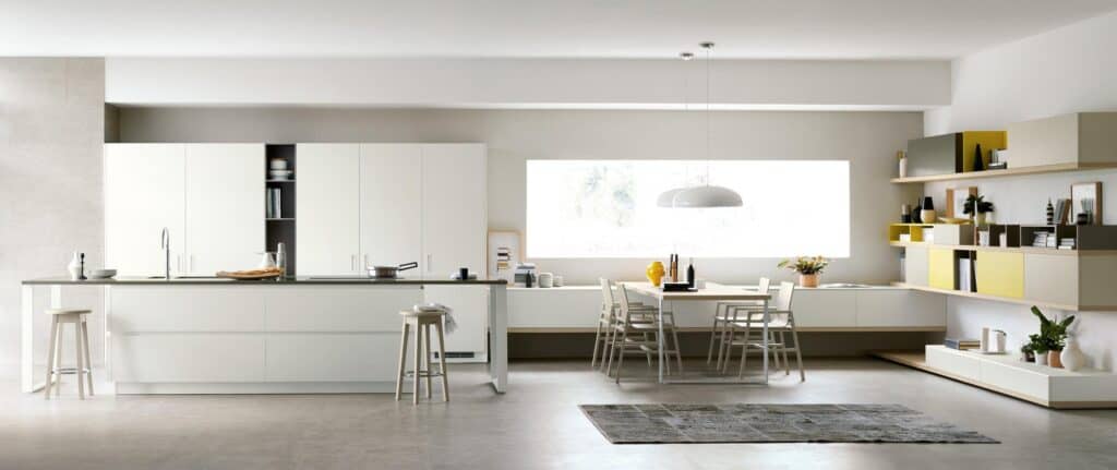 Modern kitchen and dining area with white cabinets, a central island, stools, a table with chairs, large window, and minimalist shelves.
