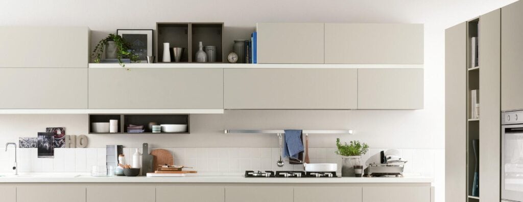 Modern kitchen with beige cabinets, white countertops, gas stove, and wall-mounted open shelves featuring decor items and plants.