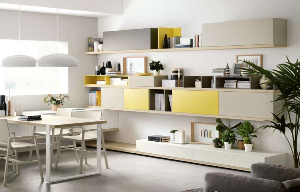 Modern dining room with white and yellow wall shelves, a wooden table with chairs, pendant lights, and decorative plants.