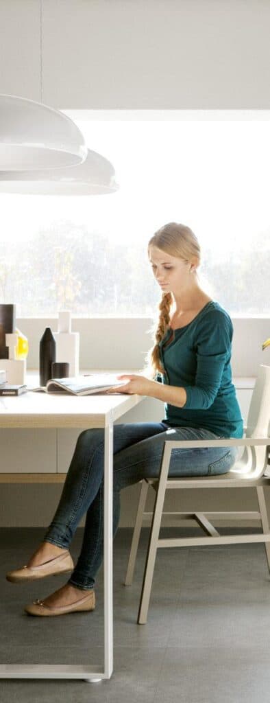A woman sitting at a table in a bright room, reading a document.