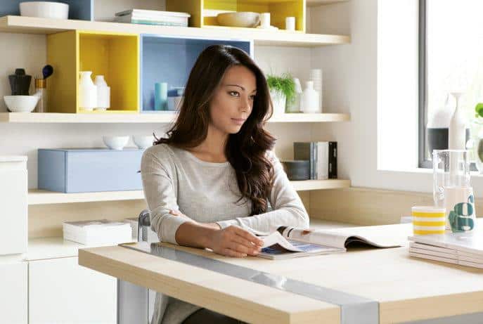 A woman sitting at a table in a modern, cozy room, looking thoughtful while flipping through a magazine.