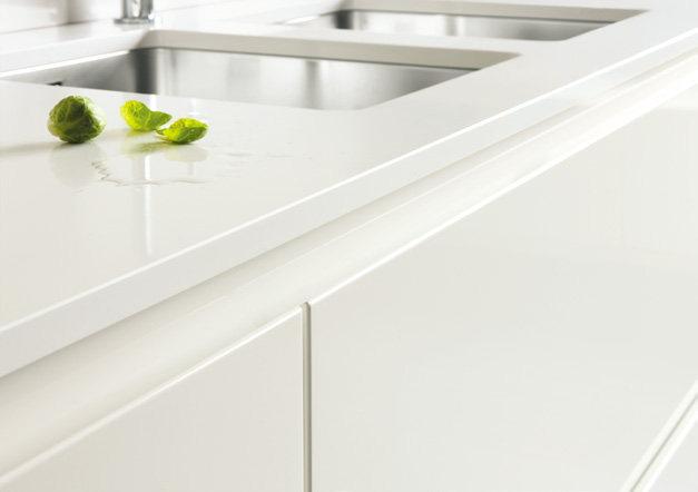 White kitchen countertop with a stainless steel sink and water droplets near small green leaves.